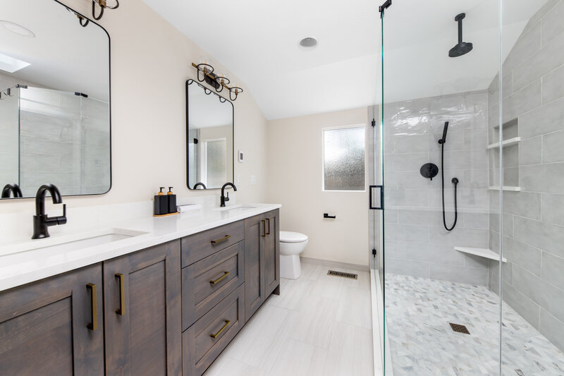Modern bathroom with dark wood double vanity, white quartz countertops, and frameless glass shower featuring matte black fixtures—designed by Belle Design Collective in San Diego.