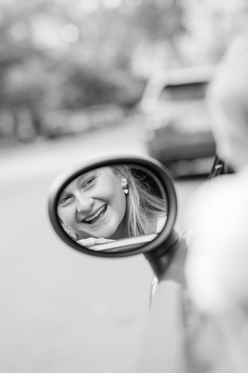girl smiling in her car's side mirror