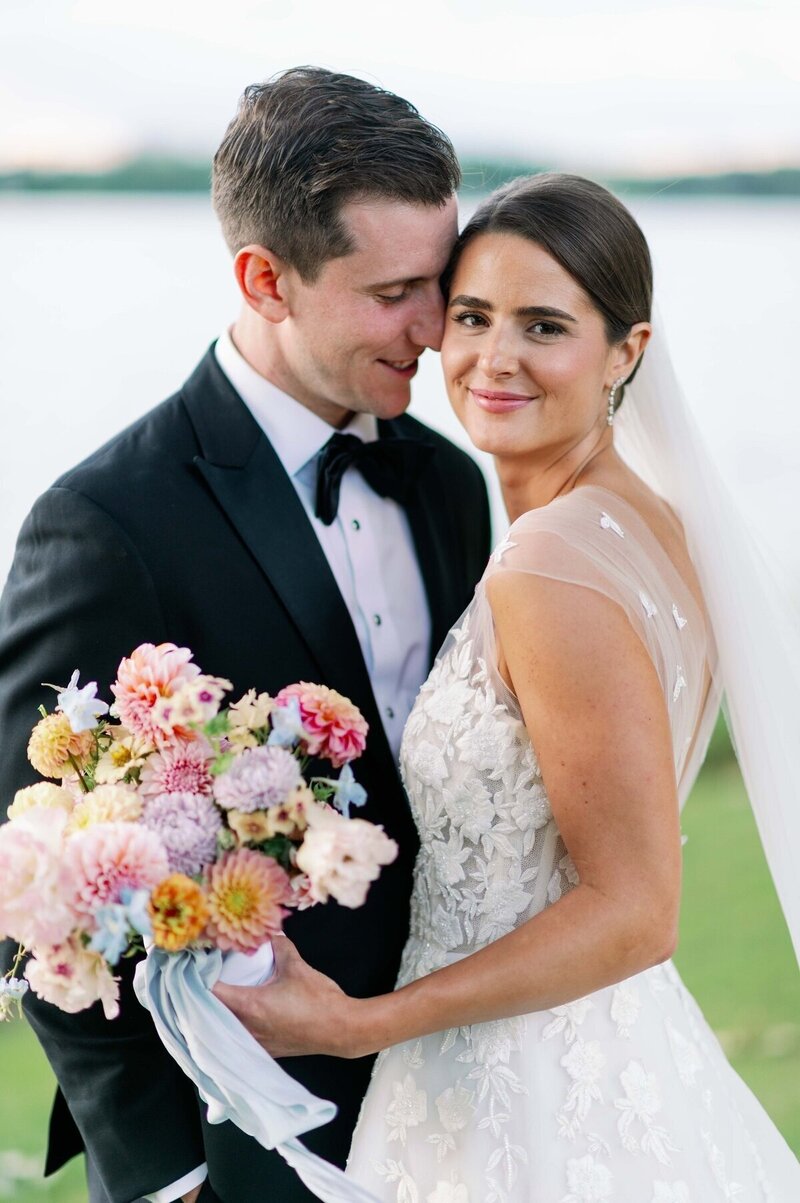 bride holding bouquet gazing happily at camera while groom presses face into hers smiling for minneapolis wedding photographer