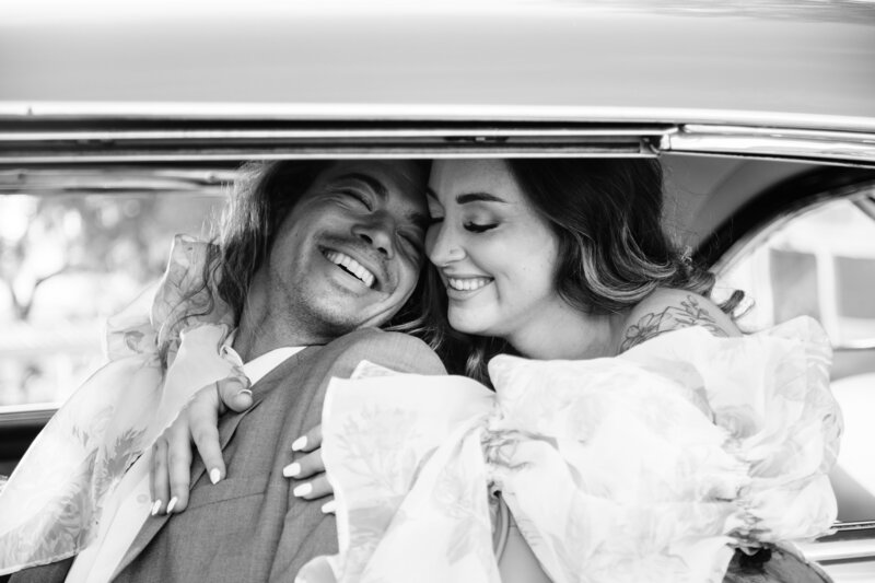 Romantic black and white photo of bride and groom inside a vintage, laughing and snuggled together