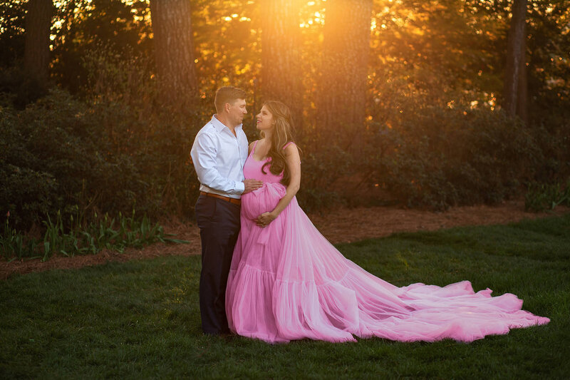 Expectant couple at WRAL Azalea Gardens with sunset behind them