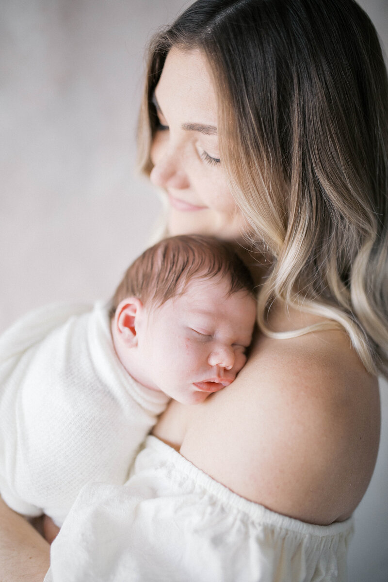 Newborn Portrait taken in a studio in Jacksonville with the mother in a creamy long dress while the baby snuggles on her shoulder