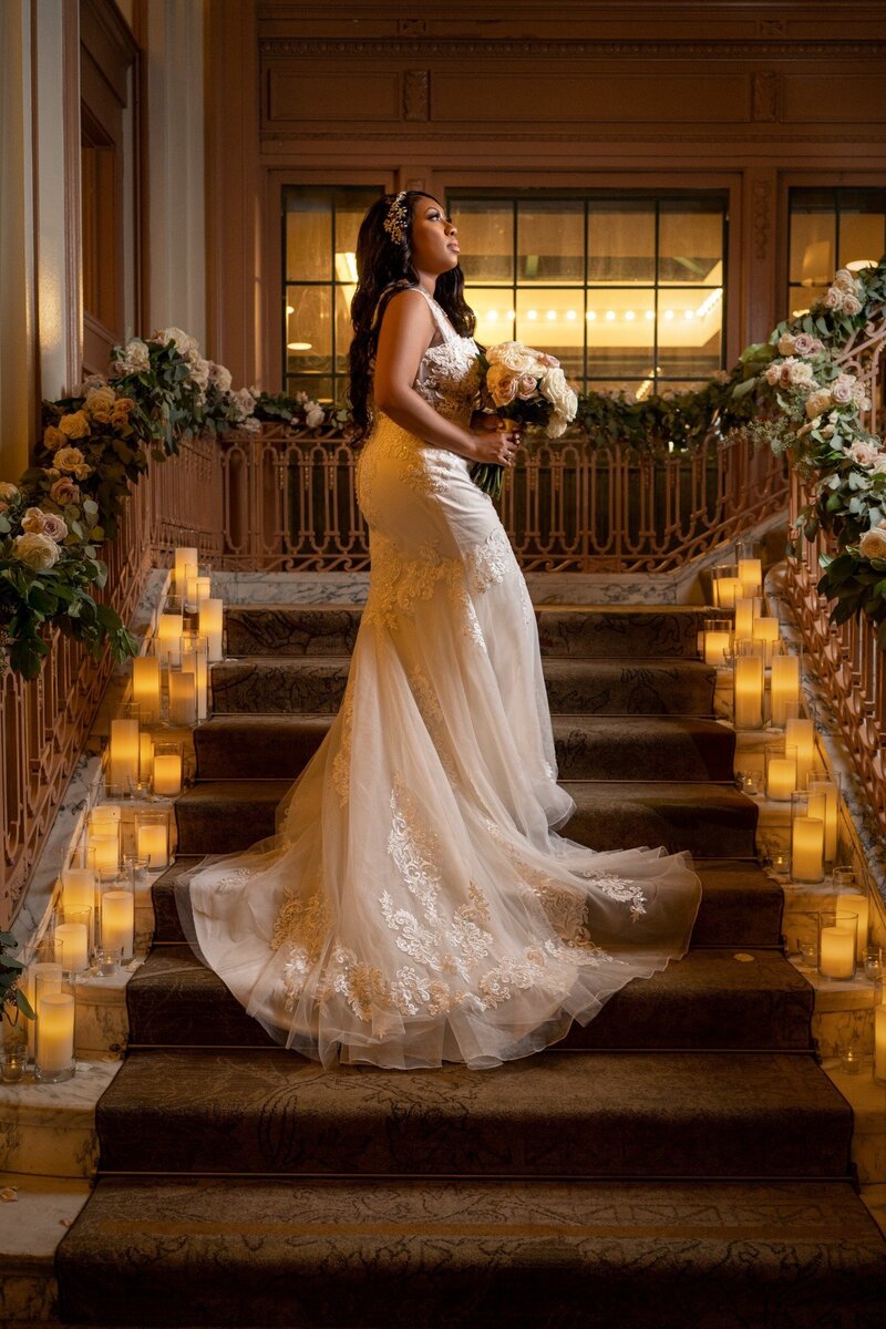 Bride in lace gown holding bouquet on candlelit grand staircase at Omni Hotel in downtown Indianapolis