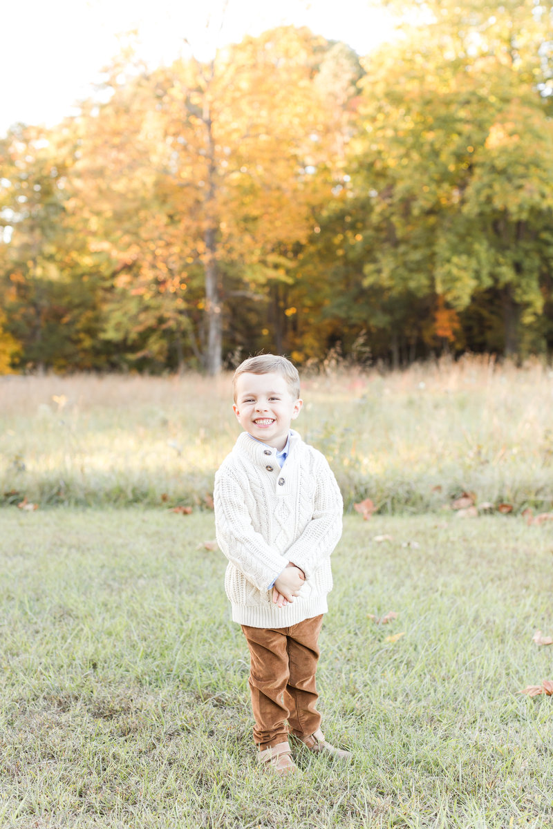 A DC Family Photographer photo of a young boy smiling at the camera while wearing a cute knit sweater and khaki pants in the Fall