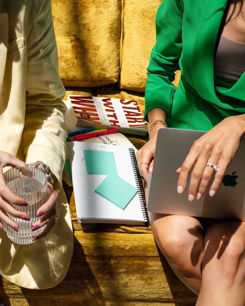 woman in business clothes holding high heels and sitting on the arm of a yellow couch