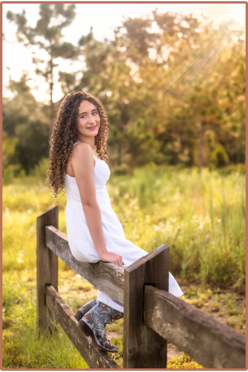 Girl sitting on a wooden fence in a grassland