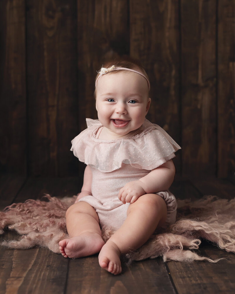 Girl sits for her milestone session in pink onesie while sitting for his milestone pictures..