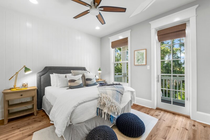 Coastal-style queen bedroom with wood floors, private balcony access, and tropical views at Cottage Ct rental on 30A.