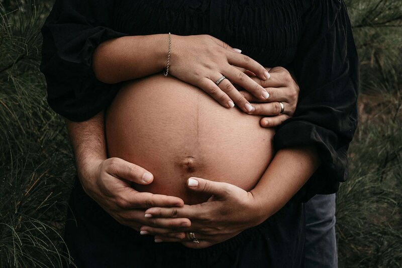 A tender moment with a pregnant woman and her partner, hands resting on her belly, symbolizing support and love during the fertility coaching journey.