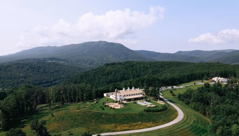 Aerial view of a large estate amidst rolling hills with forested mountains in the background, a perfect scene captured by a Destination Wedding Photographer.