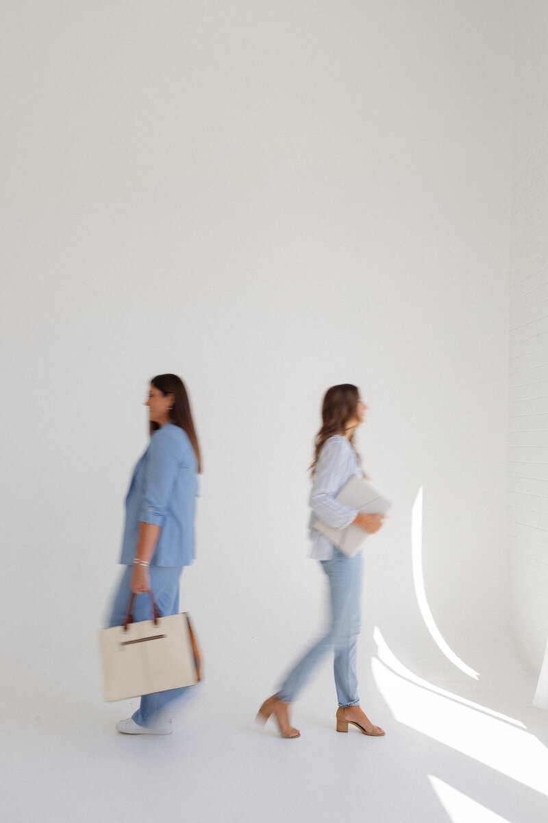 Blurry image of Melinda and Chancey, the team behind Fancy Chancey in San Diego CA, walking in front of a white studio wall