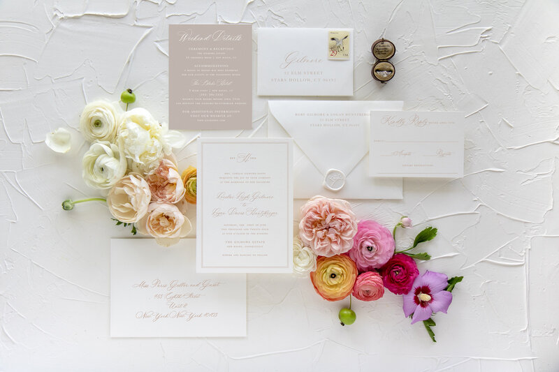 a flat lay of a tan and white wedding invitation suite
