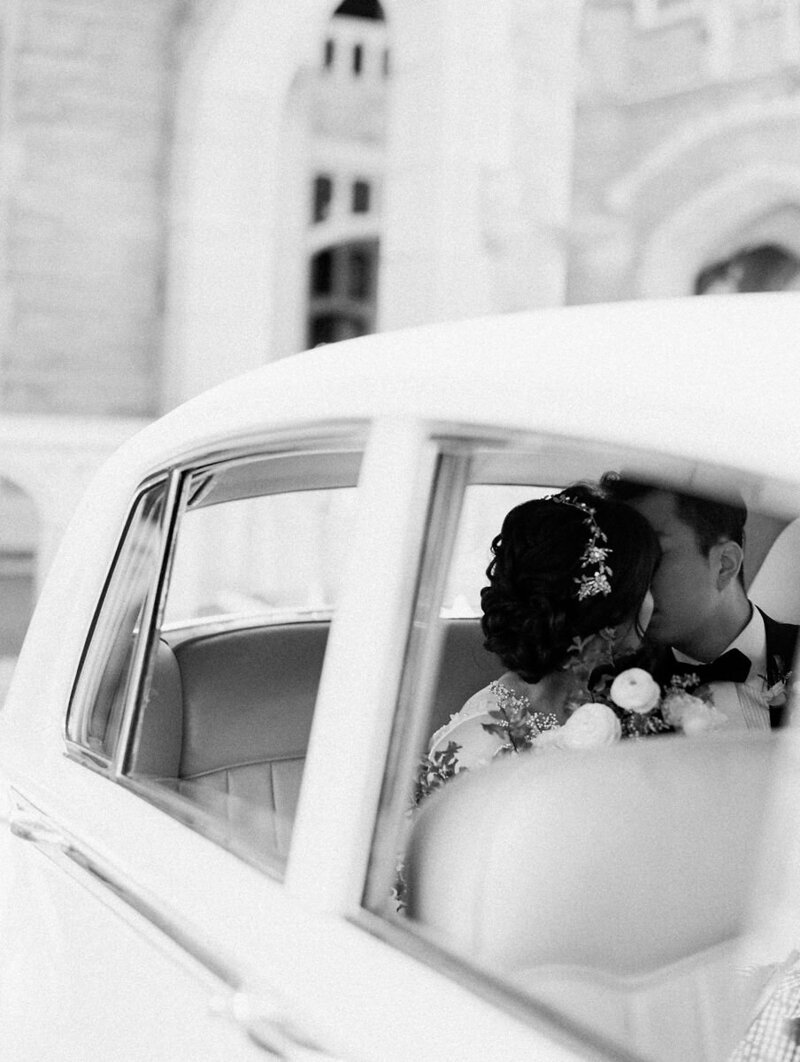 black and white photo of couple kissing in backseat of a white luxury car