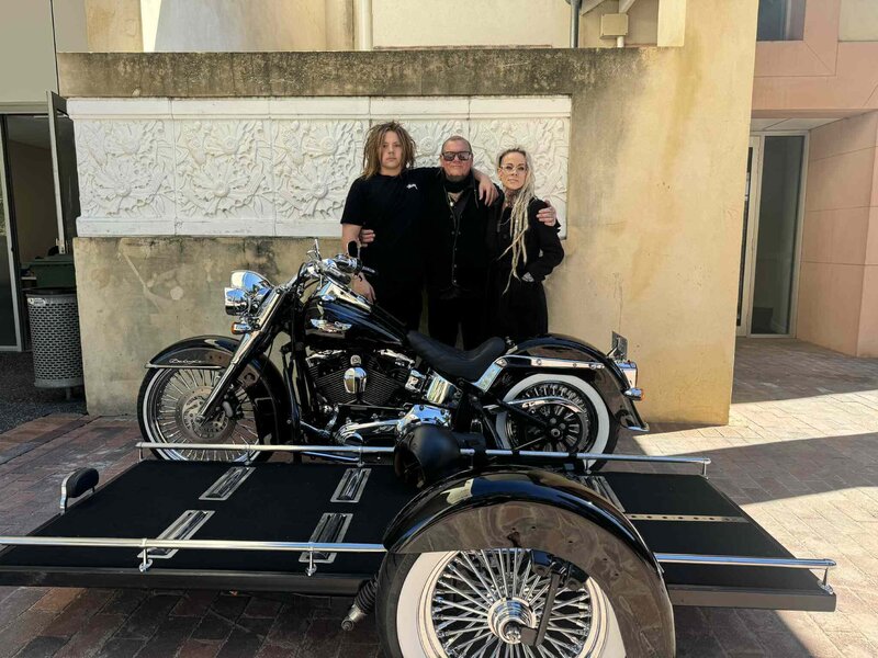 Ben, Kristy and their son standing proudly behind the Harley Davidson hearse, representing Caskets and Chrome’s family-owned service in Perth.