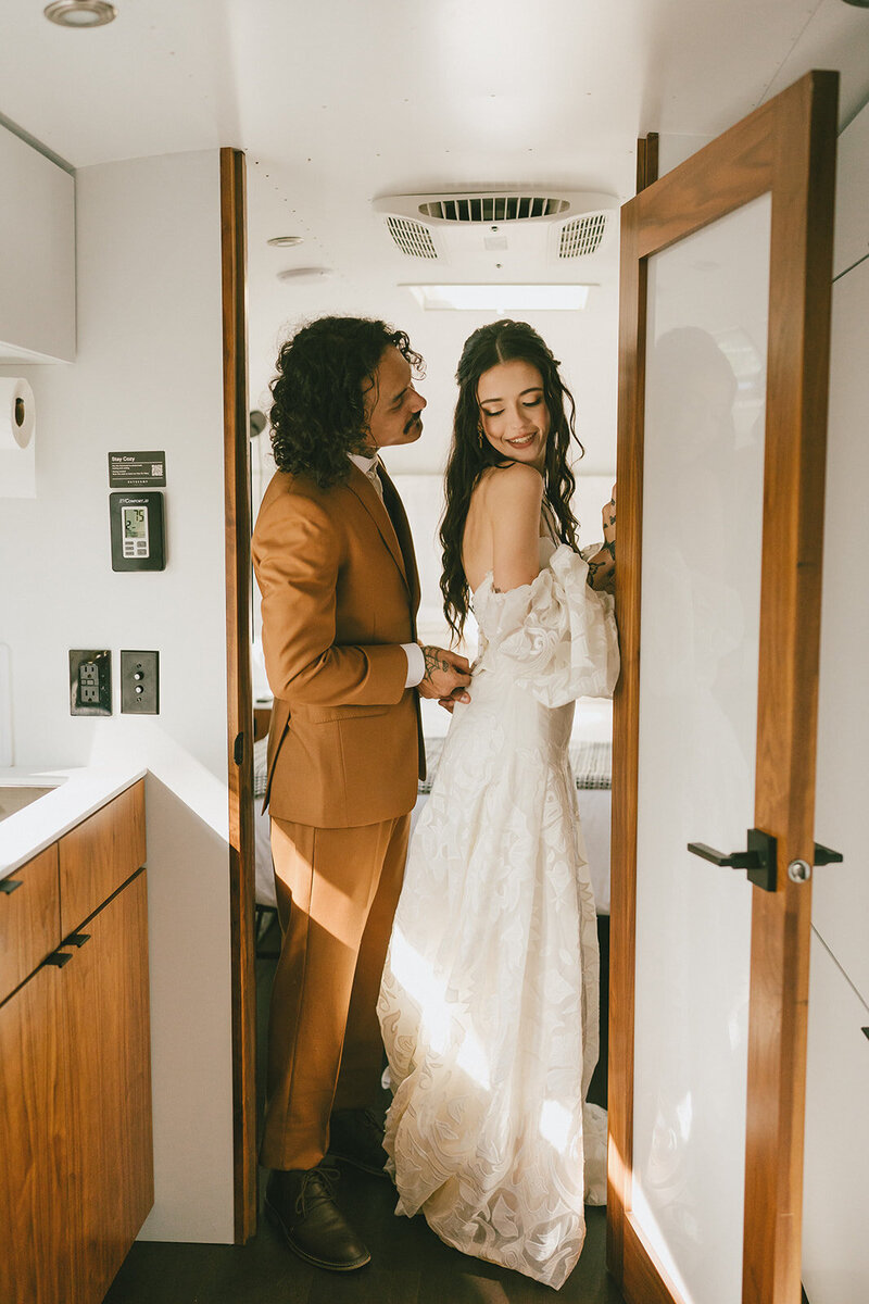 groom helps zip brides dress