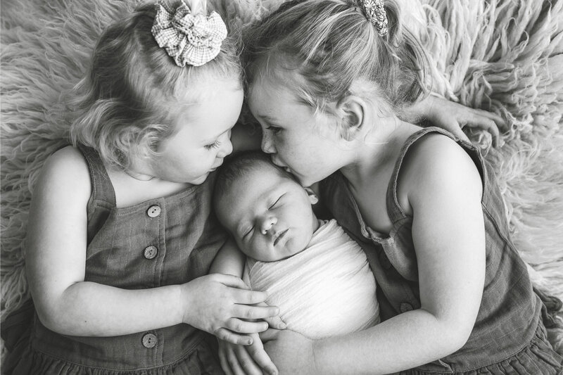2 little girls kissing their baby brother