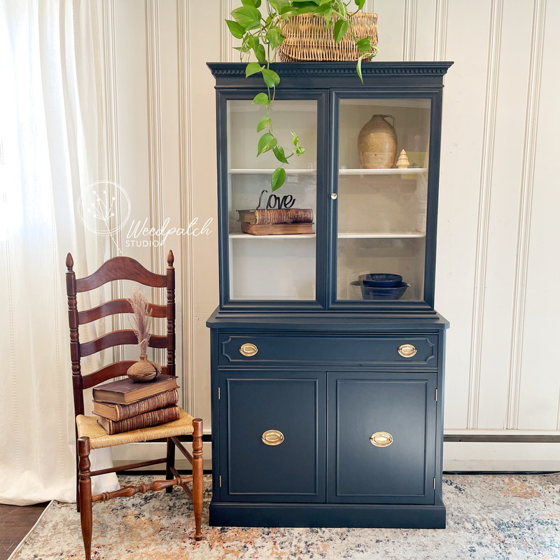 Image of a professionally refinished 1930s Mahogany China Cabinet by Weedpatch Studio. The cabinet is staged elegantly to highlight its deep navy blue color, meticulously selected and applied, showcasing the piece's timeless design
