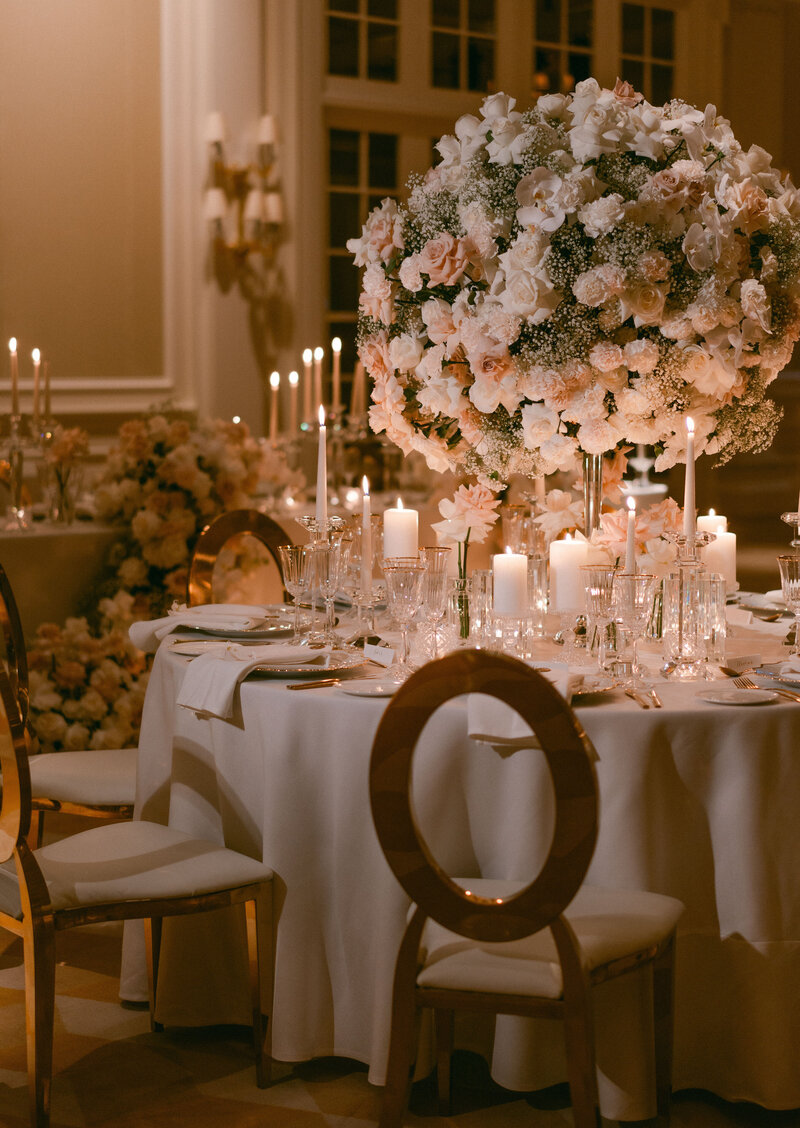 Luxurious wedding reception setup at Raffles London Hotel with elegantly decorated tables, featuring large floral centerpieces and candles.