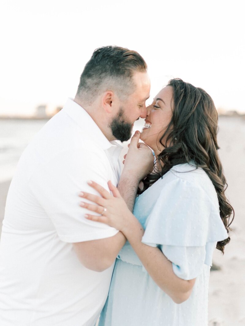 Man and woman smiling and lean in for a kiss on a beach.