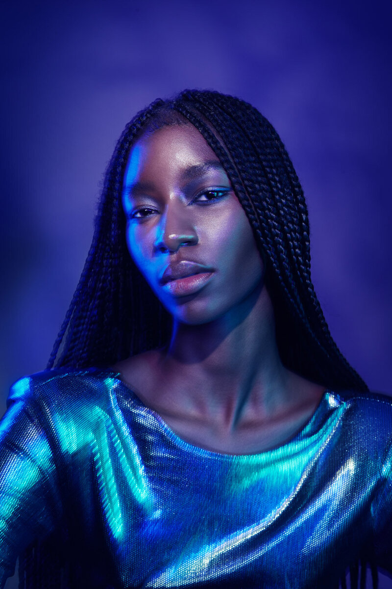 Moody studio portrait of Tracy wearing a reflective blue outfit, captured with dramatic lighting by Ylva Erevall.