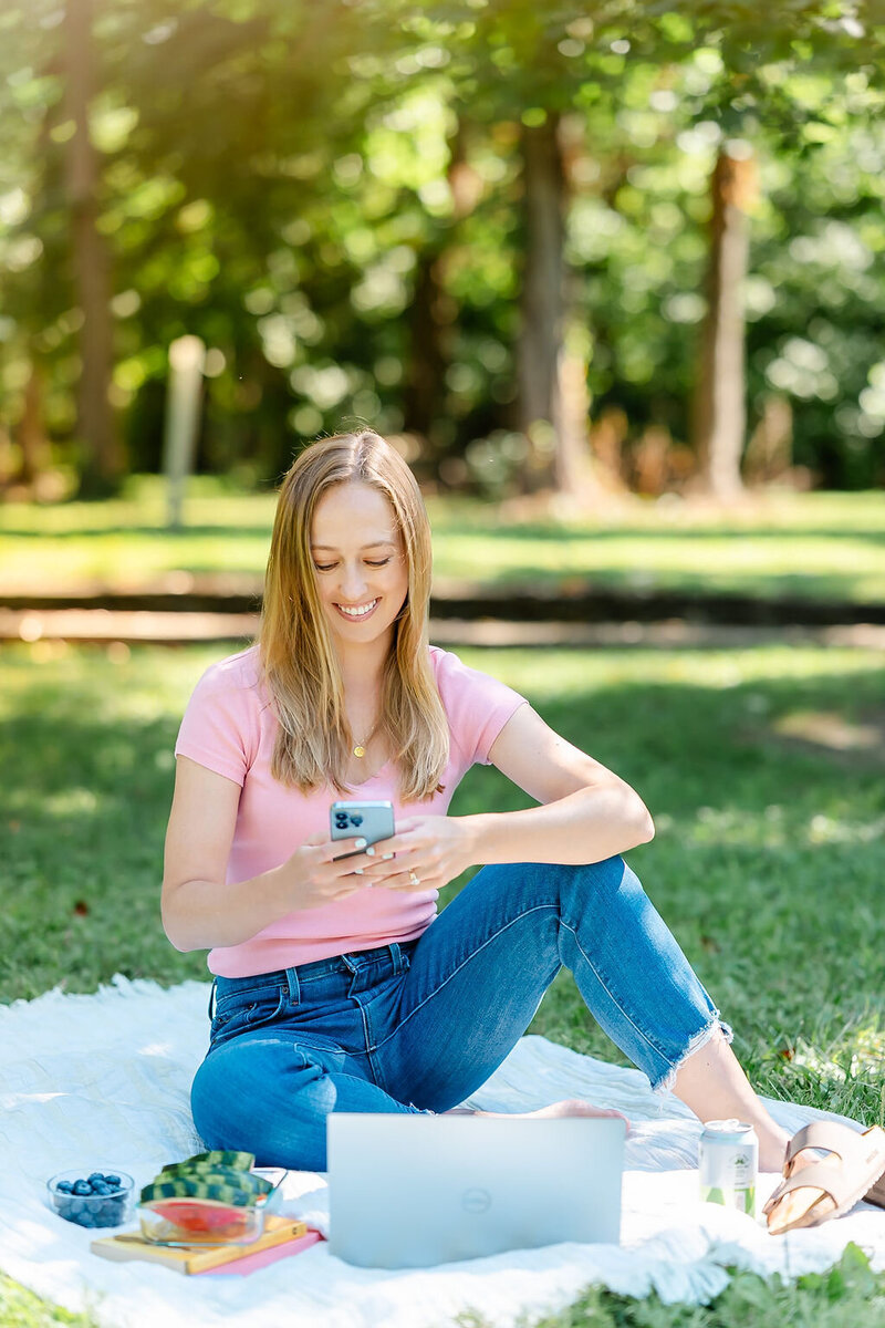 Emily working in a park on her cell phone, helping her clients get more inquiries through Pinterest