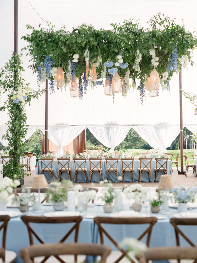 Empty tented wedding reception space with blue table linens, wooden chairs, and green, blue and white accents for a destination wedding