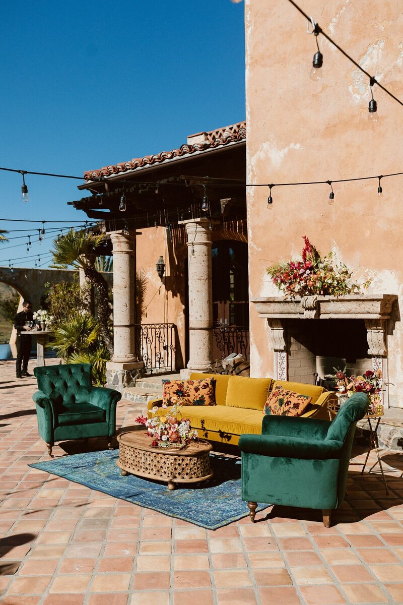 The iconic Bachelor Mansion fireplace with a yellow velvet sofa and two green velvet armchairs. A colorful lounge at a cocktail party at Villa de la vina.