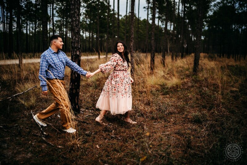 A man and woman holding hands in a forest.