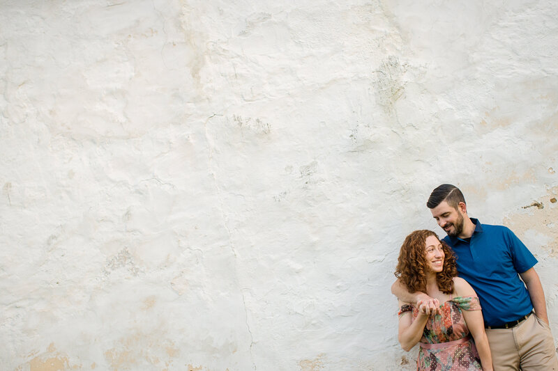 Couple sharing laughter while leaning against a white wall at Valley Forge National Historical Park during their engagement session.
