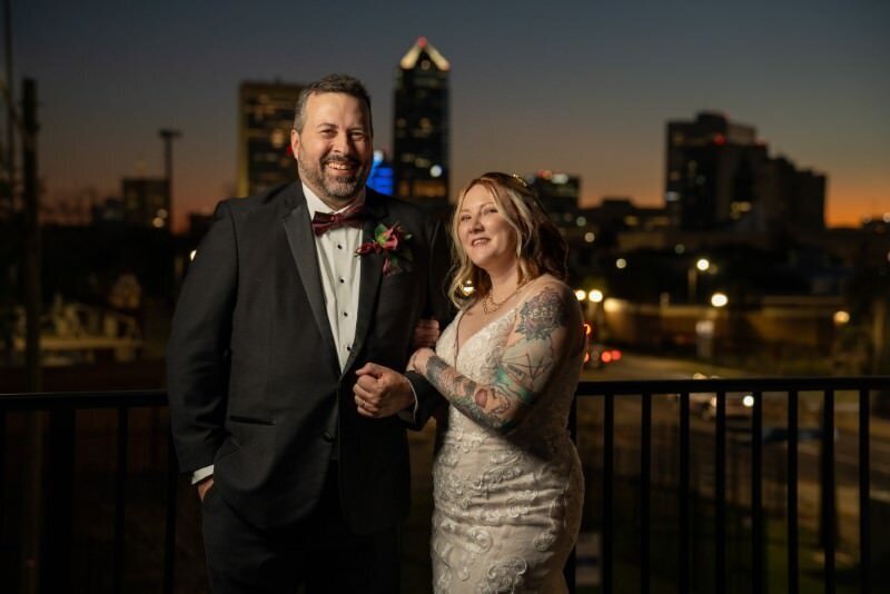 groom and bride pose with the skyline of jacksonville florida behind them on their wedding day