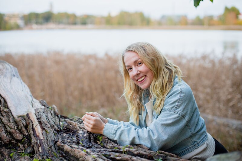 mielen paremminvoinnin ja kehomieliyhteyden valmentaja  nojaa puunrunkoon luonnon keskellä hymyillen