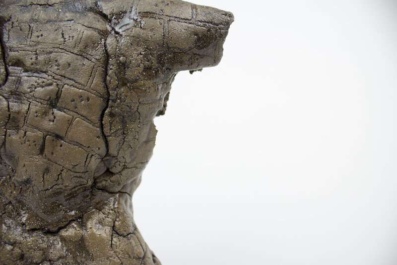 A ceramic bust of a feminine body with various cracks and brick textures