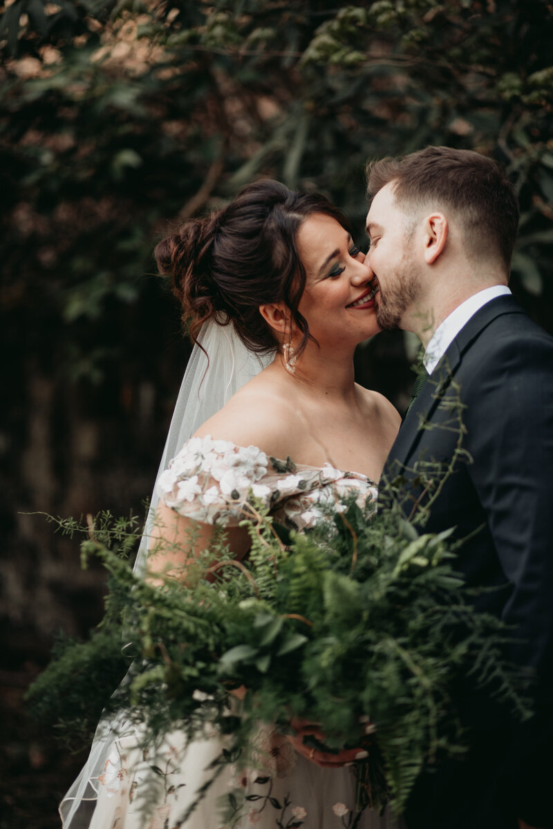 bride and groom leaning in for a kiss in the woods