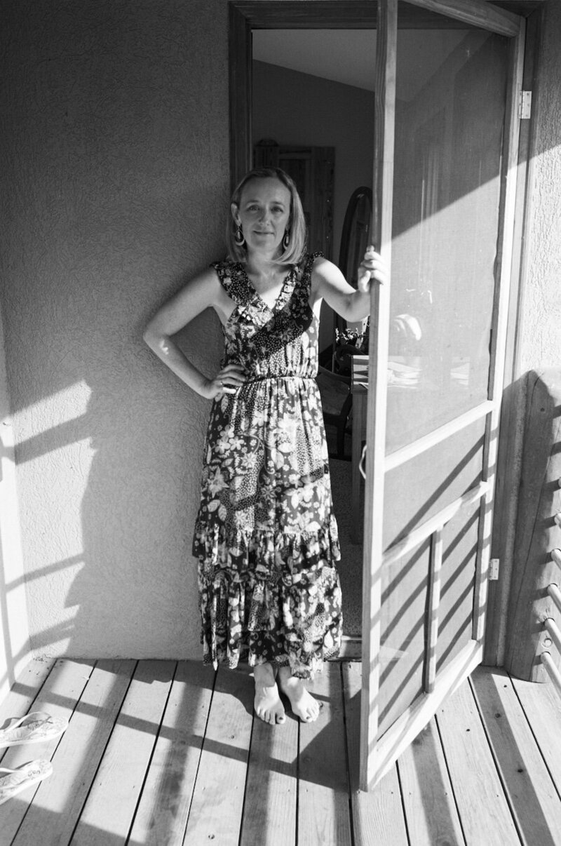 black and white portrait of a woman standing by a screen door