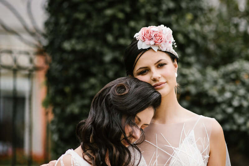 Two brides hugging, wearing wedding dresses and floral headpiece