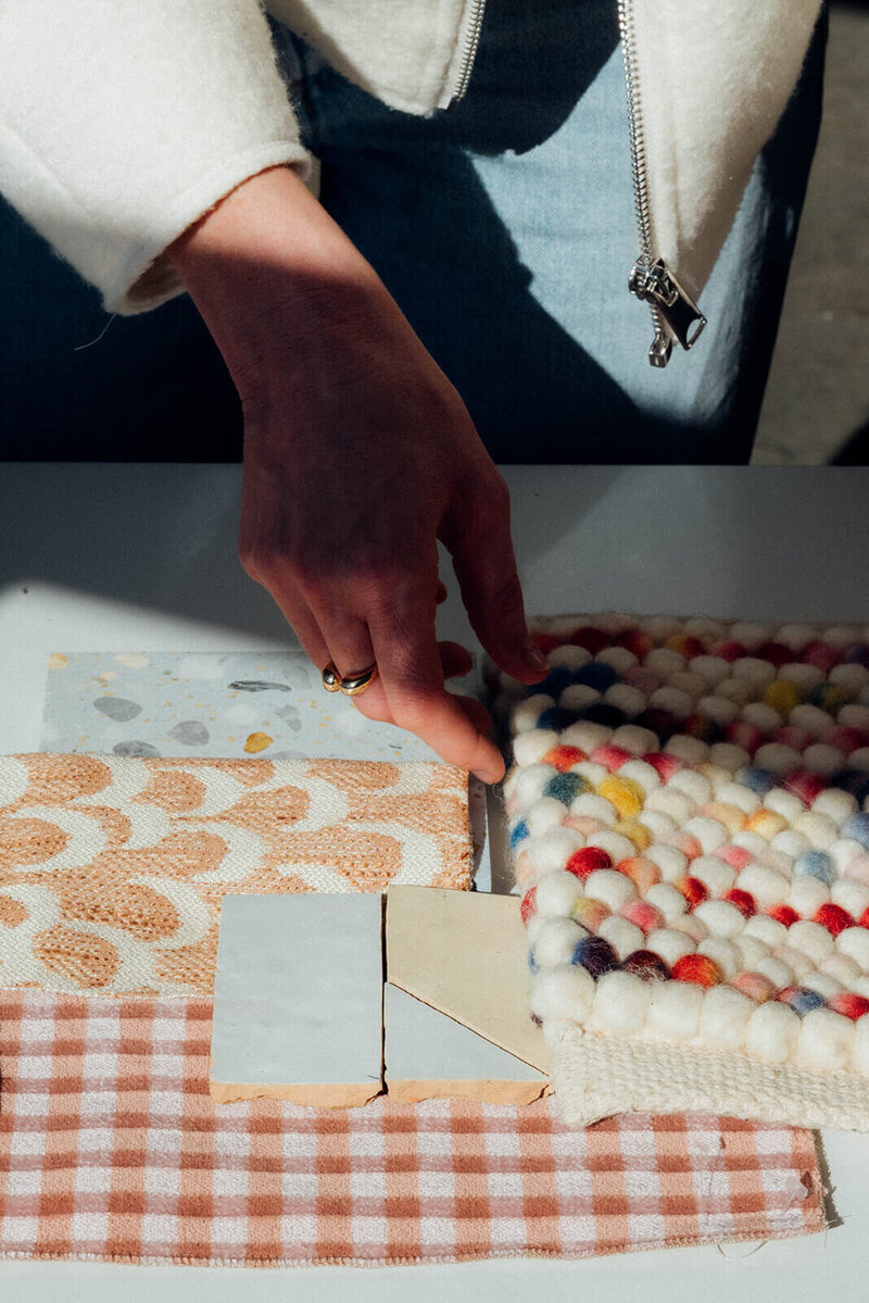 A closeup of a hand placing sample fabrics and color swatches on a table, representing the eclectic home decor style of Winsome Home Interiors.