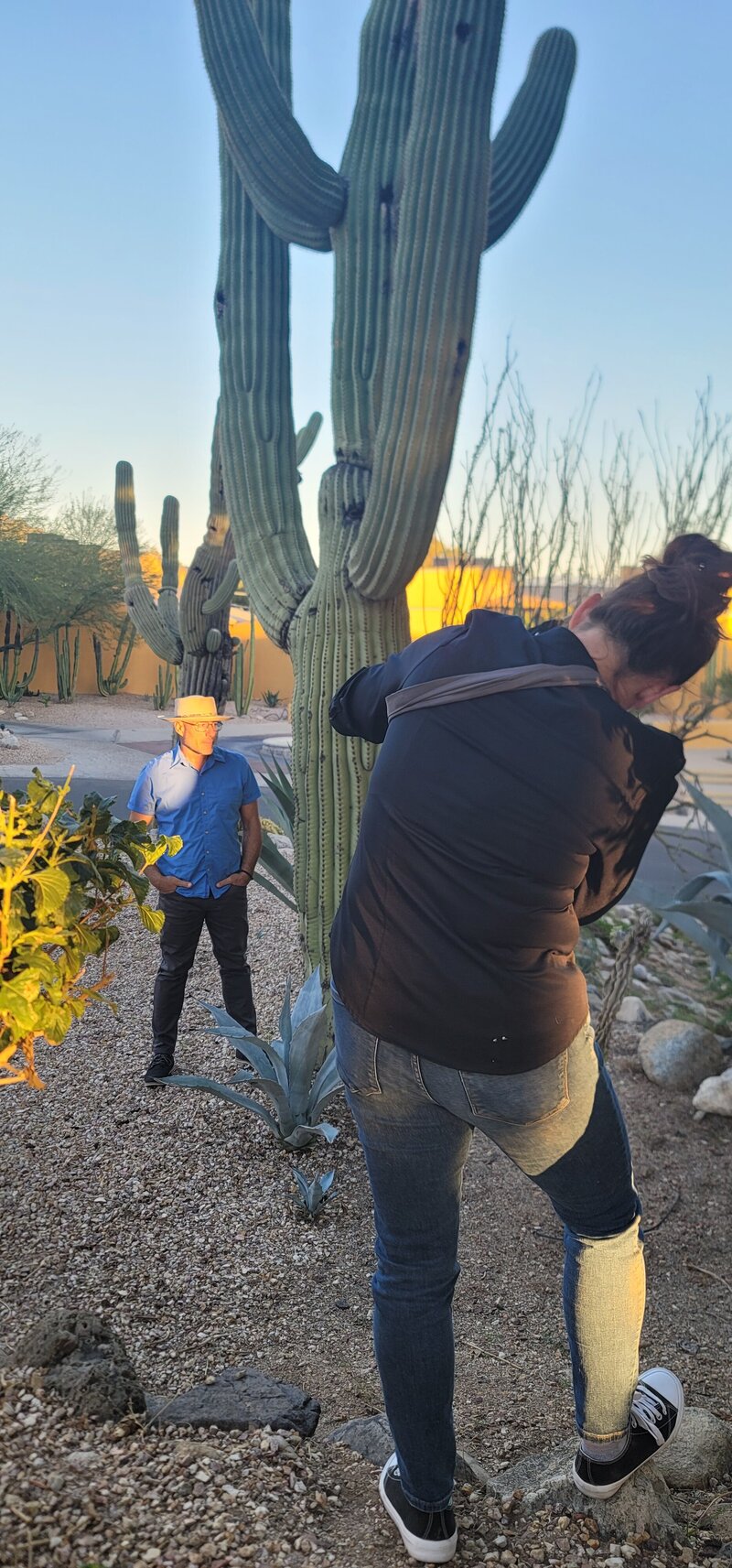 Candid outdoor moment of a man standing near desert plants while a photographer captures the shot, photographed by Vyrl Photo, showcasing Tucson brand photography.