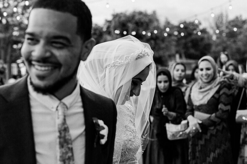 A newlywed couple smiles as they do the Zaffa while family watches