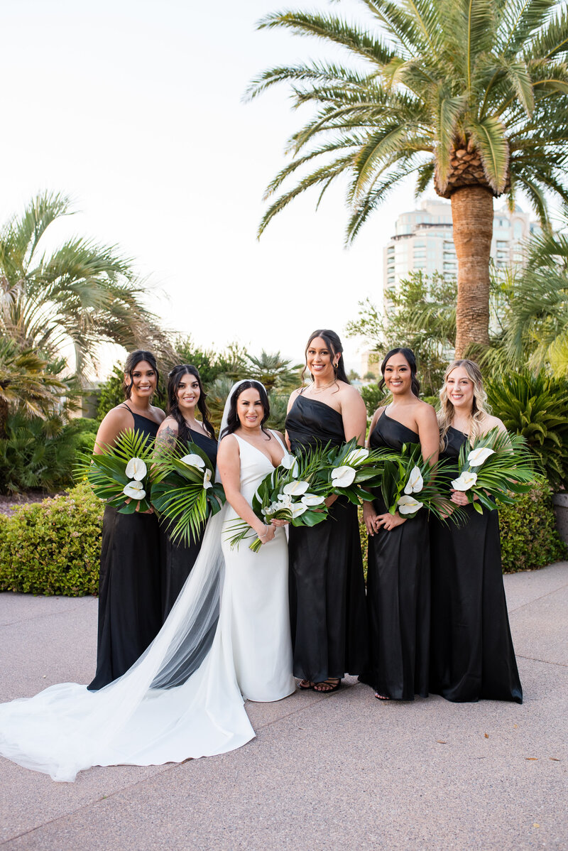 Bridesmaids in black dresses holding green and white bouquets by Jennifer’s Floral Designs.