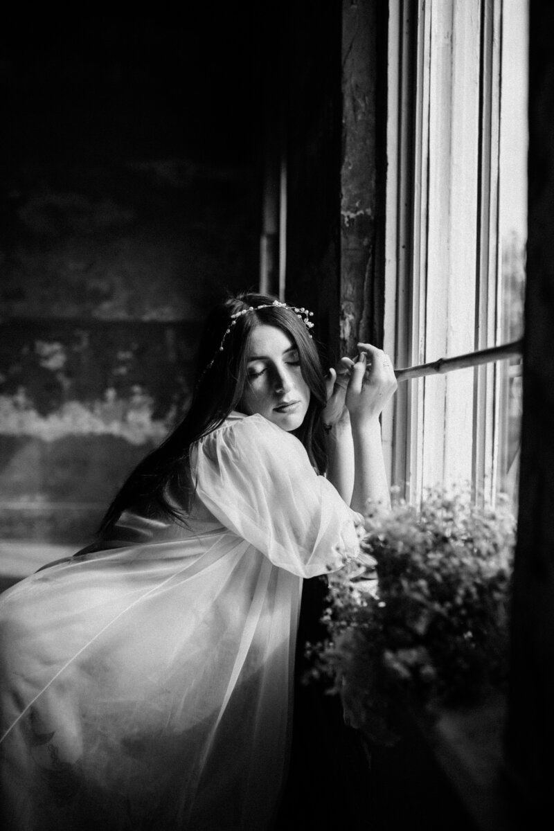 black and white image woman leaning on window sill with flowers