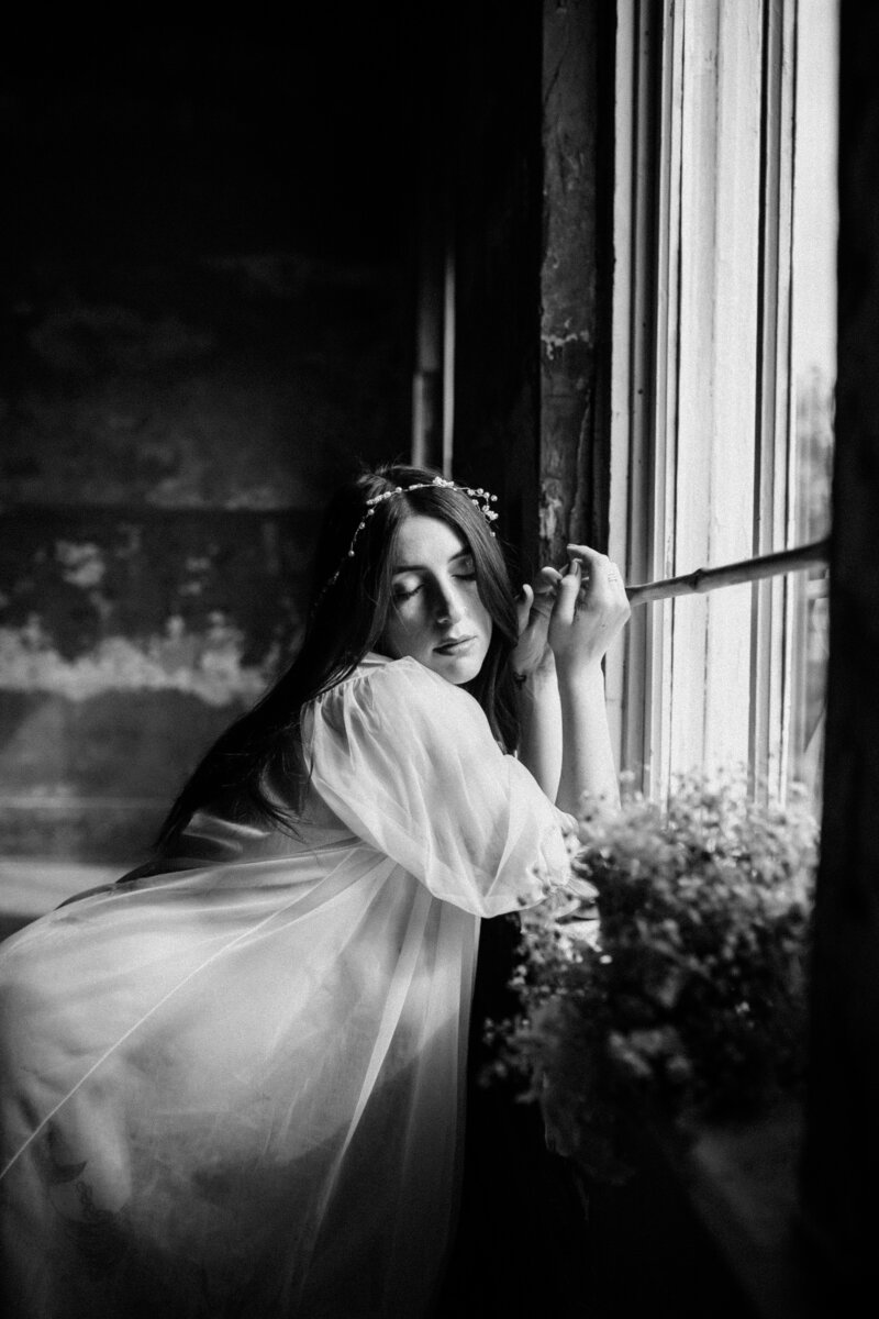 black and white image woman leaning on window sill with flowers