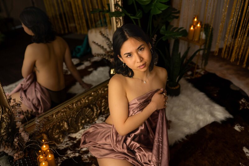 woman in red lingerie and flower tattoo on shoulder laying on bed with white sheets with eyes and mouth closed and one hand on her neck gently resting