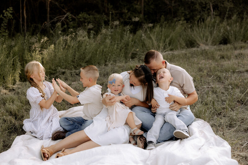 family sitting on a white blanket playing with their children.