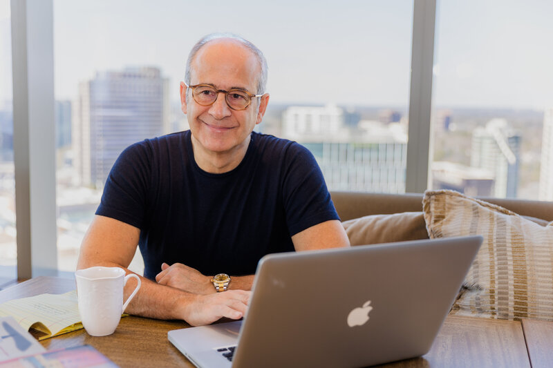 Ahmet Bozer wearing a black t-shirt, attending a meeting in front of big windows with towers in the background during his Atlanta Buckhead session
