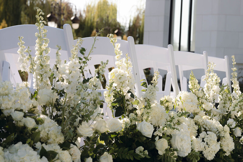 Close-up of white floral arrangements lining the ceremony aisle, showcasing an editorial wedding photographer’s refined style and sophisticated decor.