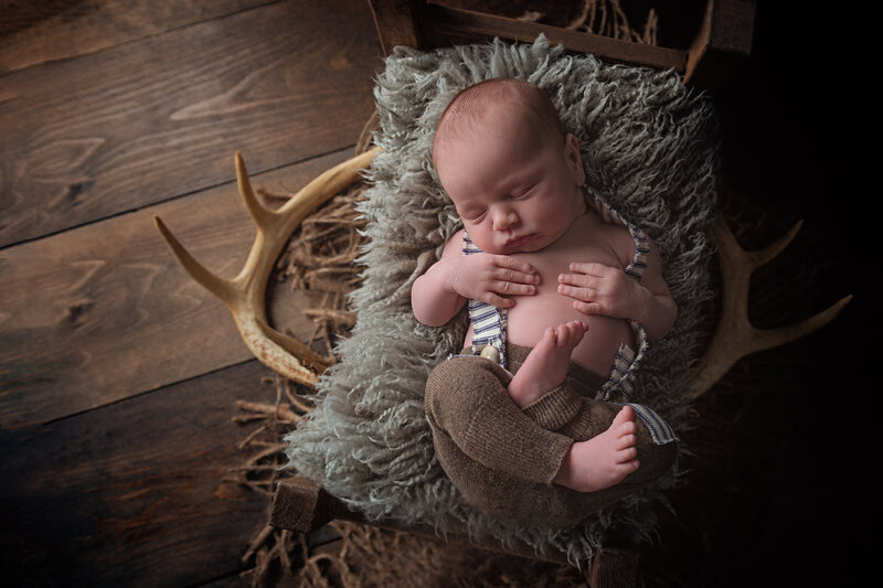 Blending rustic charm and vintage warmth, this newborn portrait features striped suspenders, antlers, and cozy textures.