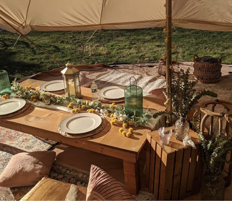 Boho-style picnic setup with wooden tables, lanterns, citrus accents, and textured pillows under a canopy, styled by Yours Truly, a wedding planner and designer in New Jersey.