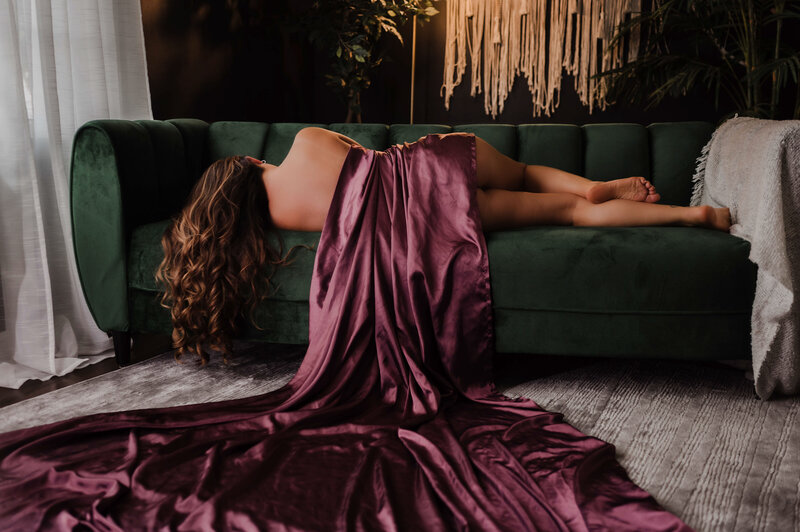 A woman laying across a green couch while covered in a purple sheet in a Memphis Boudoir Photography studio