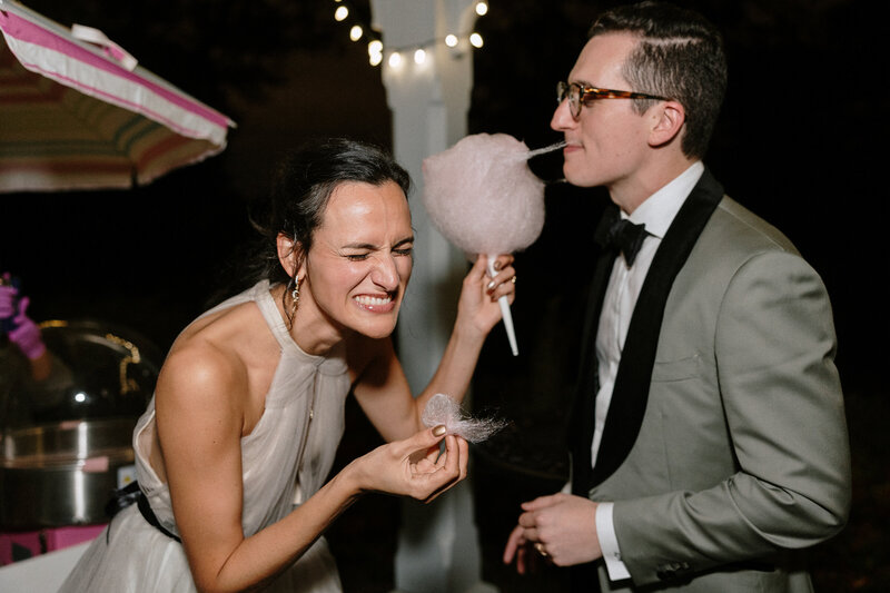 A joyful bride and groom share a lighthearted moment while laughing at a whimsical cotton candy treat.