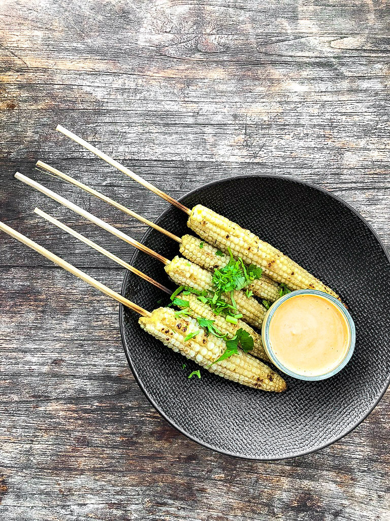 A photo five ears of corn on sticks with parsley on top.